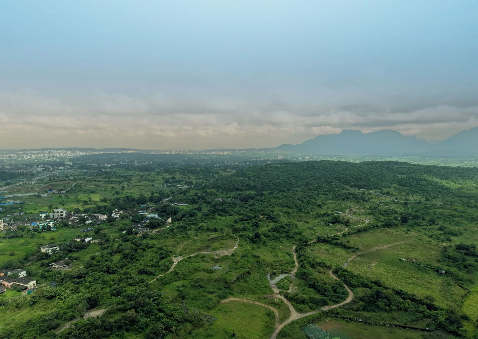 The outlook from the Haware Swaraj site at Davdi Gaon over green hill country toward the Dombivli skyline, photographed November 2025